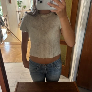 Beige ribbad croppad topp - Glittrig vit stickad topp. Köpt second hand i Köpenhamn. Står L i tröjan men skulle säga att det är S/M.