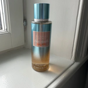 Victoria's Secret Bare Vanilla Splash - Fräsch body mist från Victoria's Secret i doften Bare Vanilla Splash. Flaskan är i blått och guldigt glas med metallic-finish och rymmer 250 ml. Doften har inslag av kokosblomma, iriserande lotus och vanilj. Perfekt för dig som gillar söta och tropiska toner. Ny