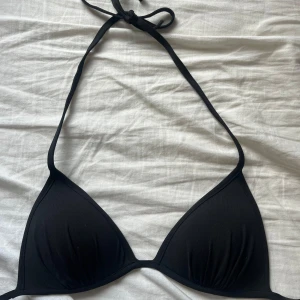 Svart trekantsbikini från H&M - Svart trekantsbikini från H&M i klassisk modell med knyt i nacken. Enkel och stilren design som passar perfekt till stranden eller poolen. Tillverkad i mjukt och stretchigt material för en bekväm passform.