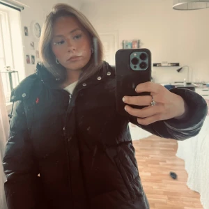 Svart pufferjacka från Polo Ralph Lauren - Säljer en svart matt pufferjacka från Polo Ralph Lauren med ikonisk röd logga på bröstet. Jackan har hög krage, dragkedja och tryckknappar framtill. Jätteskön och perfekt till höst och vinter! 