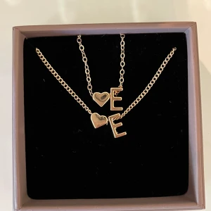 Guldigt halsband & armband med hjärta och E - Säljer ett matchande set med halsband och armband i guld. Båda har en tunn kedja med berlock i form av ett hjärta och bokstaven E. Perfekt för dig som vill ha något personligt och stilrent. Nyskick🤩