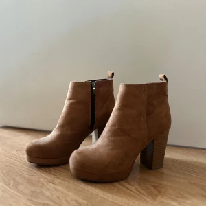Bruna mocka stövletter med klack - Snygga bruna stövletter i mocka med kraftig klack och plattform. Skorna har rund tå och dragkedja på sidan för enkel påtagning. Perfekta för dig som vill ha en stilren och trendig look till höst och vinter.
