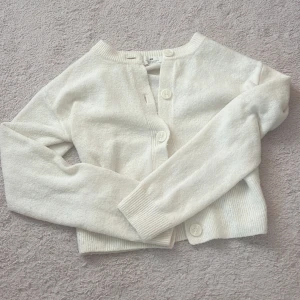 Vit kofta från H&M med knappar - Superfin vit kofta från H&M med rund halsringning och stora knappar framtill. Långärmad modell i mjukt material med ribbade muddar och nederkant. Perfekt att slänga över en topp för en clean look.