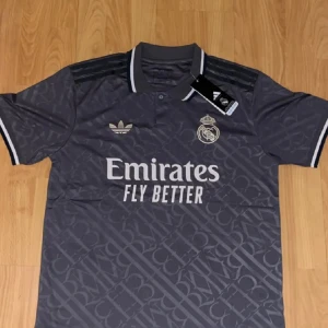  Grå fotbollströja - Snygg svart Real Madrid fotbollströja från Adidas med diskret mönster och vita detaljer på krage och ärmslut. Tröjan har klubbmärke och Adidas-logga på bröstet samt 'Emirates Fly Better' tryckt framtill. Tillverkad i lätt och ventilerande polyester.