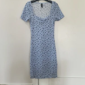 Blommig ljusblå kortklänning H&M Divided - Supersöt ljusblå kortklänning från H&M Divided med små mörkblå blommor, ribbad struktur och lätt rynk vid bysten. Klänningen har korta ärmar och en feminin v-ringning. Perfekt för sommarens alla tillfällen!