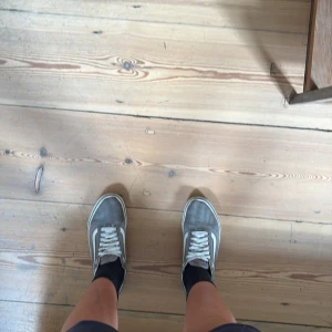 Gråa Old Skool sneakers - Säljer ett par klassiska  Old Skool sneakers i grå mocka med vita detaljer och snörning. Skorna har den ikoniska vita sidoremsan och platt sula. Perfekta för dig som gillar en clean och tidlös streetstil.