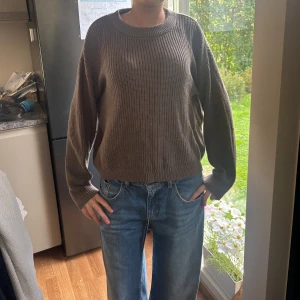 Brun stickad tröja med rund hals - Säljer en brun stickad tröja med rund hals och avslappnad passform. Tröjan har långa ärmar och ribbade muddar vid ärmslut och nederkant. Perfekt för lager-på-lager och chill dagar.