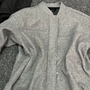 Grå kappa från Gina Tricot XS - Säljer en stilren grå kappa från Gina Tricot i storlek XS. Kappan har en rak passform, dold knappslå och lång ärm. Perfekt att slänga över en t-shirt för en chill look. Materialet känns mjukt och lite tjockare, vilket gör den extra mysig.