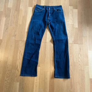 Levi's 506 blå jeans W33 L34 - Klassiska Levi's 506 jeans i blå denim med raka ben och normal passform. Snyggt mellanblå tvätt, femficksmodell och ikonisk läderpatch bak i midjan. Perfekta för dig som gillar tidlös stil och vill ha ett par jeans som funkar till allt.