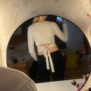 Vit ribbad topp med knyt från NA-KD - Säljer en vit ribbad långärmad topp från NA-KD i storlek S. Toppen är croppad med snygg öppen rygg och knytband bak. Perfekt för dig som gillar trendiga detaljer och vill ha en stilren men ändå unik look.