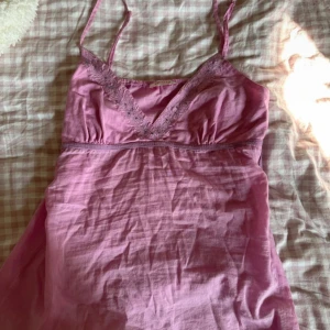 Rosa kortklänning från Orsay - Supersöt rosa top från Orsay med tunna axelband och v-ringning. Topen har broderade spetsdetaljer och små paljetter längs urringningen. Tillverkad i mjuk bomull, perfekt för varma dagar.