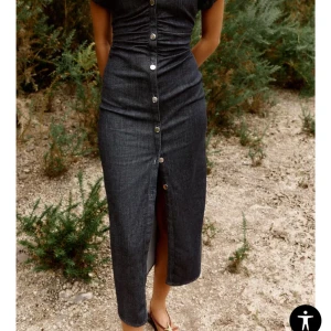 Svart jeansklänning med knappar - Snygg svart långklänning i jeansmaterial med markerad midja, korta ärmar och knappar hela vägen framtill. Klänningen är från Zara och är i storlek M. Använt en gång