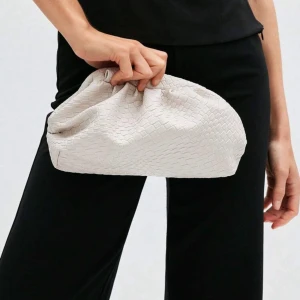 Beige clutch - Snygg beige kuvertväska med flätad struktur och mjuk, puffig form. Väskan har en lång axelrem så du kan bära den crossbody eller i handen. Perfekt för att lyfta din outfit med en trendig touch.