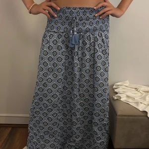 Blå långkjol från Gina Tricot - Superskön blå långkjol från Gina Tricot med elastisk smock i midjan och knytband med tofsar. Kjolen har ett snyggt mönster i olika blå nyanser och vitt, perfekt för en chill och somrig vibe.