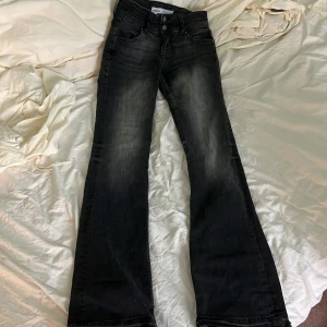 Svarta bootcut jeans från Bershka - Snygga svarta jeans från Bershka i bootcut-modell med lätt slitning på låren. Jeansen har klassisk femficksdesign, dubbla knappar i midjan och är tillverkade i stretchig denim för en bekväm passform.