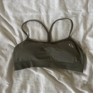 Olivgrön sportig linnetopp från Hanna öbergs märke  - Säljer en olivgrön linnetopp från Hanna överge märke med smala axelband och brottarrygg. Toppen har ribbad kant nedtill och är perfekt för träning. Enkel och stilren design med liten logga framtill.