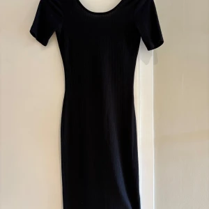 Svart ribbad klänning Gina Tricot XS - En svart, ribbad kortklänning från Gina Tricot i storlek XS. Klänningen har korta ärmar, rundad halsringning och figurnära passform. Perfekt för dig som gillar en enkel men stilren look.