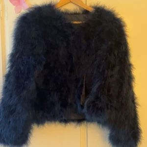 Svart pälsjacka från WOS - Fluffig svart pälsjacka från WOS med lång ärm och croppad passform. Jackan har en  mjuk och lyxig känsla med pälsimitation och knäppning framtill. Perfekt för att hålla värmen under kyliga dagar.