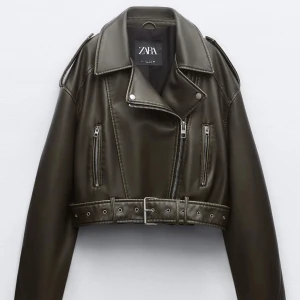 Intressekoll Olivgrön skinnjacka från Zara - Snygg olivgrön skinnjacka från Zara med dragkedja och bälte i midjan. Jackan är croppad och har långa ärmar samt flera dragkedjefickor framtill. Perfekt för en cool och edgy look!