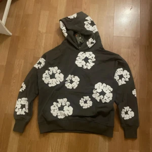 Grå hoodie med blommönster från Denim Tears - Säljer en cool grå hoodie från Denim Tears med ett unikt vitt blommönster. Perfekt design, Hoodien har en klassisk passform med långa ärmar och en bekväm huva. Perfekt för att ge din outfit en stilfull touch. Tillverkad i USA. Priset kan diskuteras!