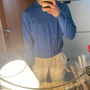 Blå tröja från Ralph Lauren - Säljer en snygg blå tröja från Ralph Lauren med deras ikoniska logga på bröstet. Tröjan har långa ärmar och en klassisk rund halsringning. Perfekt för en stilren look. Mitt pris är endast för 300 kr ett väldigt bra pris så skynda på innan den blir såld  