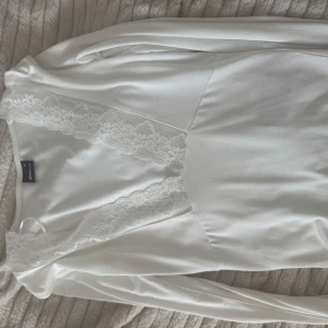 Vit långärmad topp med spetsdetalj - Säljer en stilren vit långärmad topp med v-ringad spetsdetalj. Perfekt för en elegant och bekväm look. Passar bra till både jeans och kjol! Aldrig använd.