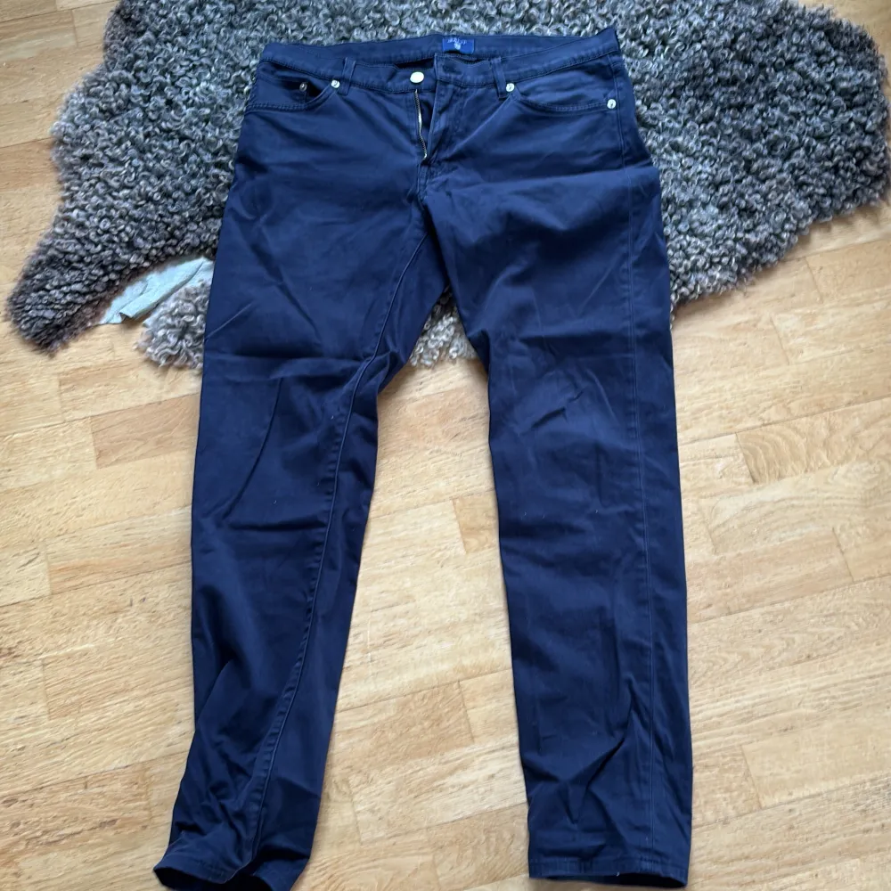 Säljer ett par mörkblå byxor från Gant i modellen slim straight. Byxorna har en klassisk design med dragkedja och knappar. Perfekta för en stilren look. W33/L32. Farkut & Housut.