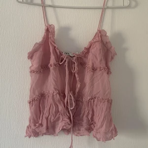 Rosa linnetopp från Zara - Söt rosa linnetopp från Zara med tunna axelband och volangdetaljer. Toppen har en knytning framtill och är perfekt för varma sommardagar. Tillverkad i ett lätt och luftigt material. Storlek M men passar som XS-S