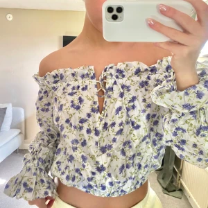Blommig offshoulder blus - Charmig blommig offshoulder blus med volangdetaljer och knytning framtill. 