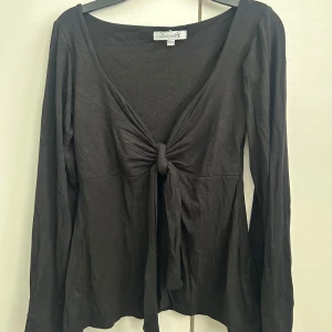 Svart långärmad topp med knyt - Snygg svart långärmad topp från DesignBySi med knyt framtill. Toppen har en djup v-ringning och är tillverkad i ett mjukt material💓