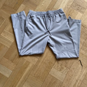 Grå kostymbyxor med snörning - Säljer ett par bekväma kostymbyxor med elastisk midja och snörning. Perfekta för en avslappnad stil. Byxorna har en normal passform och är tillverkade i ett mjukt material.