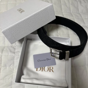 Dior bälte - Snyggt svart bälte från Dior med silverfärgat spänne. Bältet har en subtil logotypdesign och kommer i en elegant förpackning med Dior märke. Perfekt för att ge en lyxig touch till din outfit. Nytt pris 5400kr och mitt pris är 2900kr. Knappt använt har bara legat i garderoben, storlek 110cm
