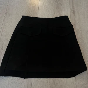 Svart kortkjol med fickdetaljer - Snygg svart kortkjol med fickdetaljer framtill.🥰