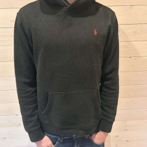 Svart hoodie från Ralph Lauren - Säljer en stilren svart hoodie från Ralph Lauren med det klassiska röda logotypen på bröstet. Tröjan har en bekväm passform med långa ärmar och en praktisk magficka. Perfekt för en avslappnad look.