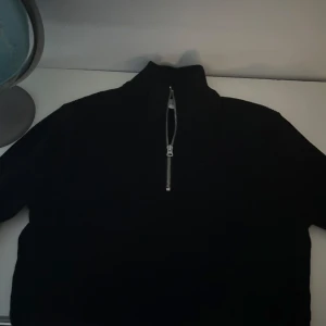 quarterzip - Säljer en stilren svart tröja med dragkedja i halsen. Perfekt för kyligare dagar och enkel att matcha med olika outfits. Tröjan har en hög krage och är tillverkad i ett mjukt material.