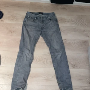 Grå jeans från Jack & Jones - Säljer ett par grå jeans från Jack & Jones med en tapered passform. Byxorna har en klassisk femficksdesign och är tillverkade i denim. Perfekta för en avslappnad stil.