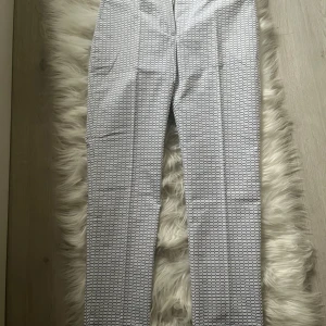 Dam Lacoste cigarette byxor - Snygga vita byxor från Lacoste med ett blått rutmönster. Byxorna har en klassisk passform som cigarette byxa dvs avsmalad och lite croppade och är tillverkade i Frankrike. Perfekta för en stilren look. Köpta i Usa, kostar $138