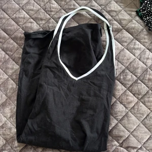 Svart ärmlös klänning från Divided - Säljer en stilren svart ärmlös klänning från Divided. Klänningen har vita kanter vid axelbanden och en enkel design som passar perfekt för olika tillfällen. Perfekt för dig som gillar en minimalistisk stil.