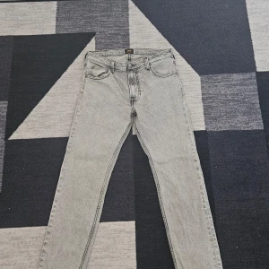 Ljusgrå jeansbyxor från Lee - Snygga ljusgrå jeansbyxor från Lee med klassisk femficksdesign. De har en rak passform och är perfekta för en stilren look. Byxorna har en dragkedja och knapp framtill.