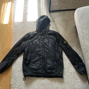 Svart vindjacka från Stone Island - Snygg svart vindjacka från Stone Island med huva och dragkedja. Mycket bra skick, säljes då den inte används längre! Storlek L