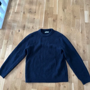 Svart stickad tröja från Nudie Jeans Co - Säljer en stilren svart stickad tröja från Nudie Jeans Co. Tröjan har en klassisk design med rund hals och långa ärmar. Perfekt för kyligare dagar och enkel att matcha med olika outfits.