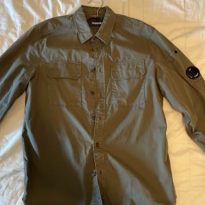Olivgrön skjorta från C.P. Company - Snygg olivgrön skjorta från C.P. Company med klassisk krage och knappar framtill. Bra skick och självklart äkta! Storlek S, passar dig som är 170-175 skulle jag säga.