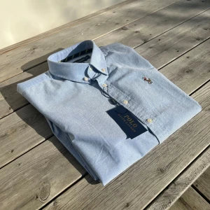 Ralph Lauren Skjorta  - Snygg ljusblå skjorta från Ralph Lauren med klassisk krage och broderad logotyp på bröstet. Skjortan har långa ärmar och knappar framtill. Perfekt för sommarn! 🤩