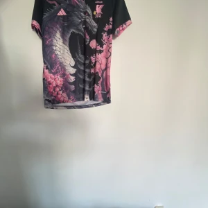 Svart och rosa fotbollströja med drakmotiv - Snygg fotbollströja från Adidas med ett coolt drakmotiv i rosa och svart. Tröjan har korta ärmar och ett unikt mönster med japanska inslag. Perfekt för dig som vill sticka ut på planen! Storlek M