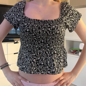 Svart och vit blommig topp från H&M - Säljer en söt svart och vit blommig topp från H&M. Toppen har korta ärmar och en smickrande fyrkantig ringning. Perfekt för en somrig look! 🌸