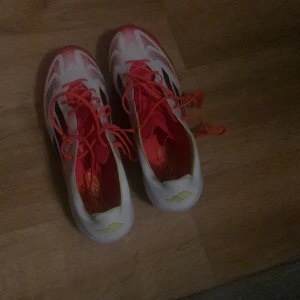 Adidas F50 fotbollsskor - Säljer ett par Adidas F50 fotbollsskor i vitt med röda och svarta detaljer. Skorna har snörning och är designade för optimal prestanda på planen. Perfekta för fotbollsspelare som vill ha både stil och funktion.