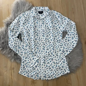 Vit blommig skjorta från Grand Frank - Säljer en stilren vit skjorta från Grand Frank med ett blommigt mönster i blått. Skjortan har en slim fit passform och är tillverkad i 100% bomull. Perfekt för en fräsch och modern look. 🌸