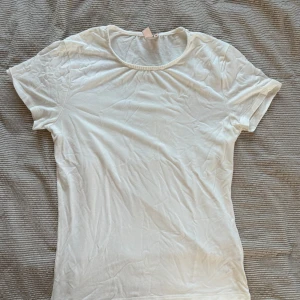Vit t-shirt från Nelly - Säljer en klassisk vit t-shirt från Nelly i storlek M. Den är kortärmad och gjord i ett mjukt material som passar perfekt till vardags. Enkel och stilren design som funkar till det mesta.