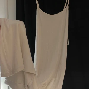 lång vit klänning gina - Säljer en elegant vit klänning med smala axelband. Perfekt för sommarens varma dagar. Klänningen har en enkel och stilren design.