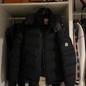 Svart pufferjacka från Moncler - Säljer en blå pufferjacka från Moncler montegenvre med dragkedja och långa ärmar. Jackan har en quiltad design och en logotyp på ärmen. Perfekt för kyliga dagar. Strl S  1 i Moncler storlek 